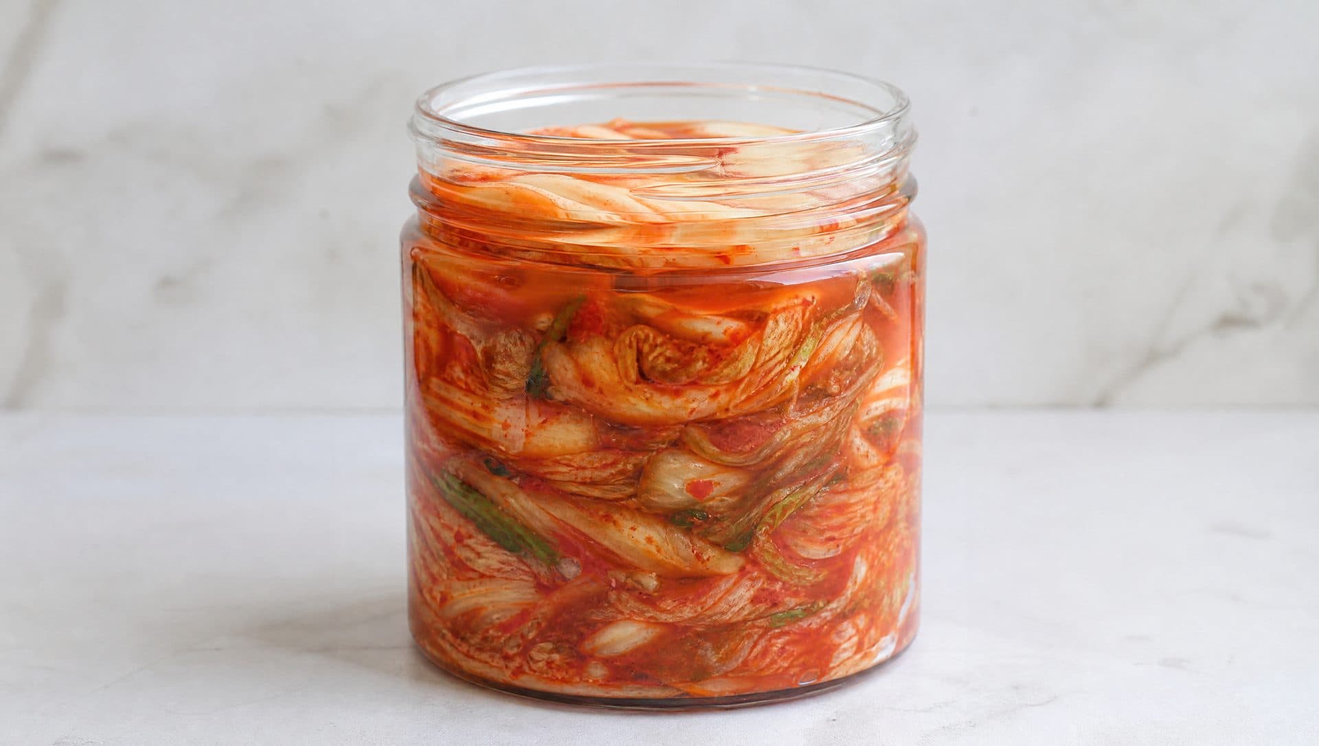 A glass jar packed with freshly made kimchi, brine rising to cover the top leaves