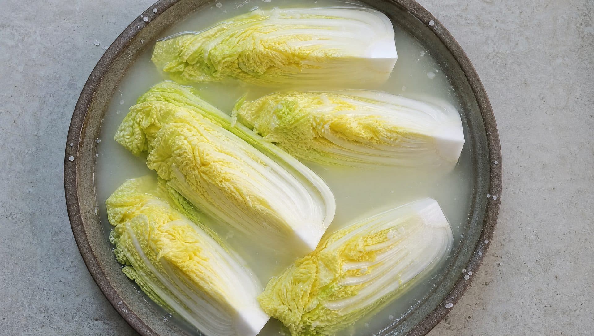 Quartered napa cabbage sitting in a wide basin of pale salt brine