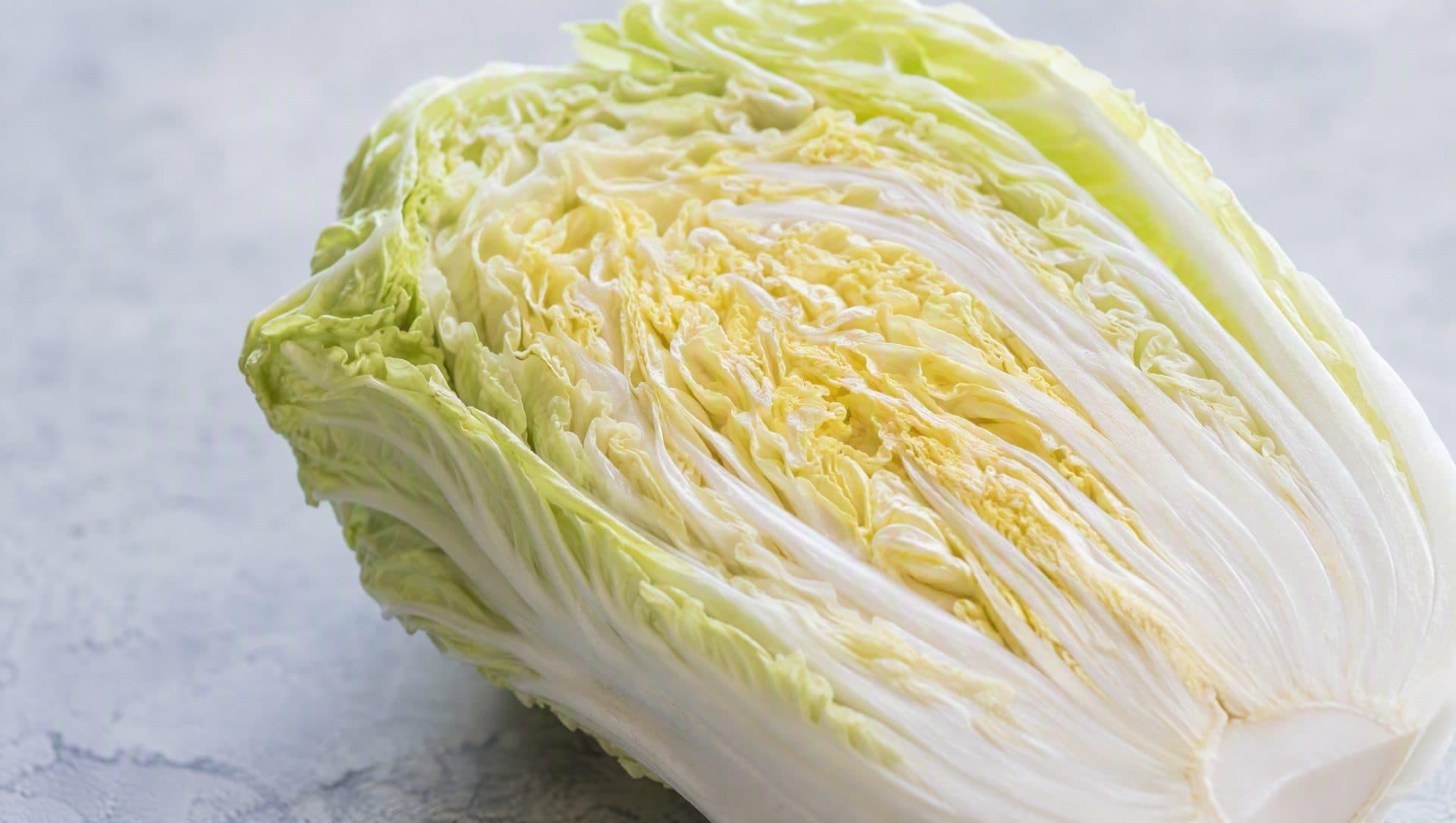 Close-up of a halved napa cabbage showing tightly packed pale yellow inner leaves and crisp white ribs