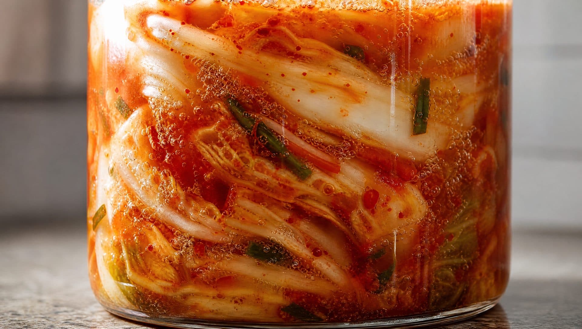 Close-up of a glass jar of fermenting kimchi with small bubbles rising through red brine